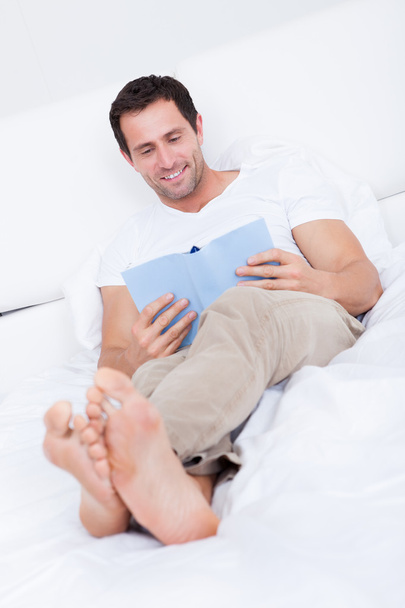 Portrait Of Young Man Reading Book On Bed - Foto, imagen