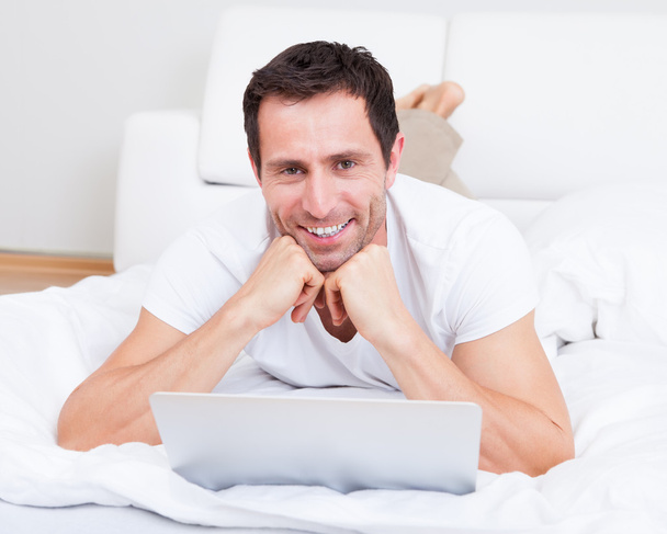 Portret van jonge man liggend op bed met behulp van laptop - Foto, afbeelding