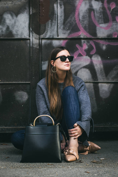 modieuze vrouw, het dragen van oversized grijze trui, spijkerbroek en beige instappers. Urban fashion blogger poseren met een zwart trendy handtas. de daling van de perfecte outfit. - Foto, afbeelding