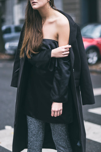 fashionable woman wearing a black oversized coat, an off the shoulder silk satin dress and glitter pants - Photo, Image