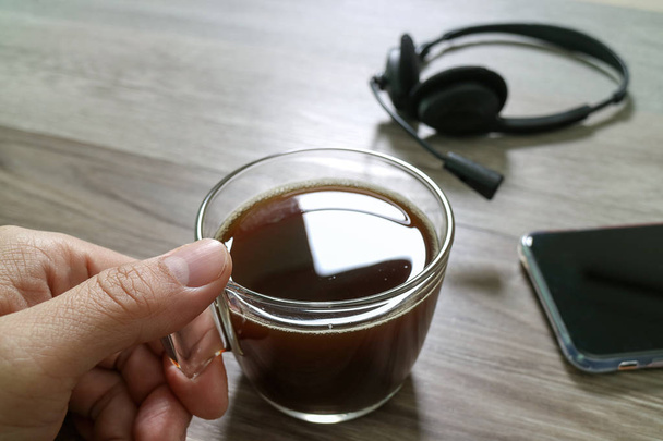 Hand hält Kaffeetasse oder Tee und VoIP-Headset, Smartphone eingeschaltet - Foto, Bild