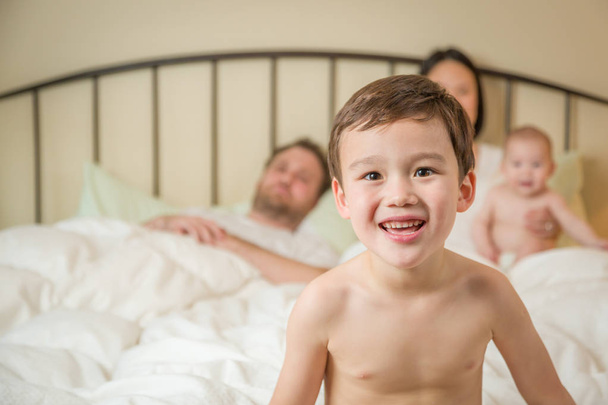 Raça mista chinês e caucasiano menino deitado na cama com sua família
 - Foto, Imagem