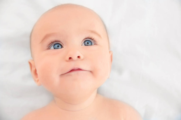 Cute baby lying on white bed sheet, close up view - Foto, Imagen