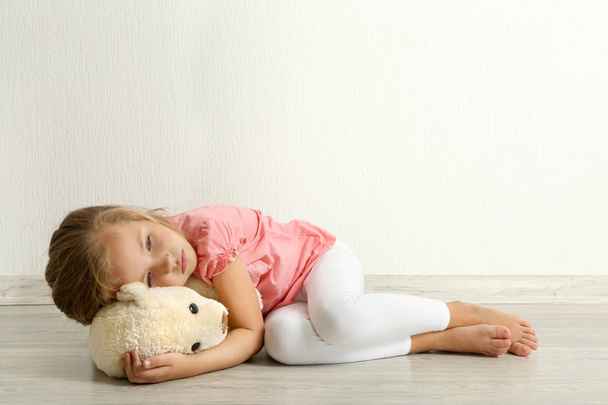 Sad little girl with teddy bear lying on floor  - Photo, image