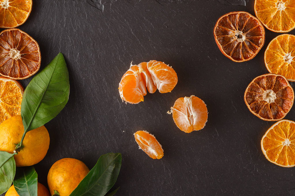 Tangerines with leaves and dry sliced orange over black slate su - Foto, imagen