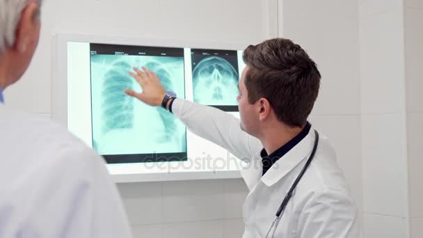 Mieslääkäri näyttää jotain röntgenkuvassa kollegalleen.
 - Materiaali, video