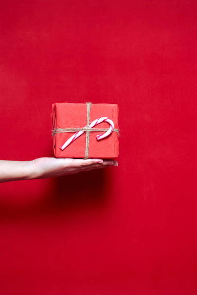 Womans hand holding a box gift with christmas lollipop on red ba - Fotó, kép