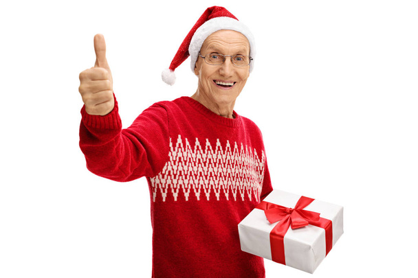 man wearing christmas hat holding present and giving a thumb up - Foto, Imagem