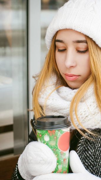 woman in white scarf and hat drinks coffee - Zdjęcie, obraz
