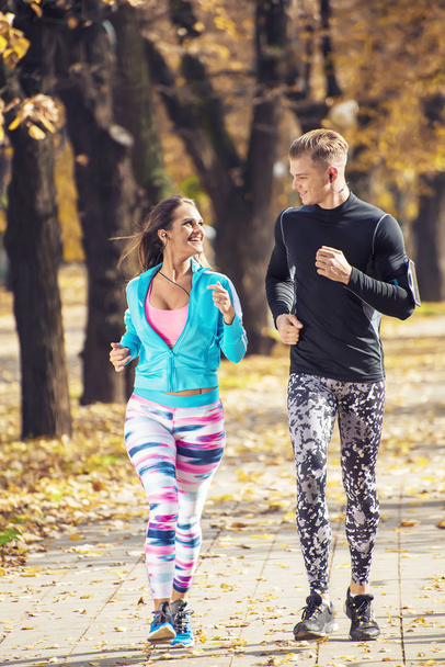 Beautiful young couple running together in the park. Autumn environment. - Foto, Imagen
