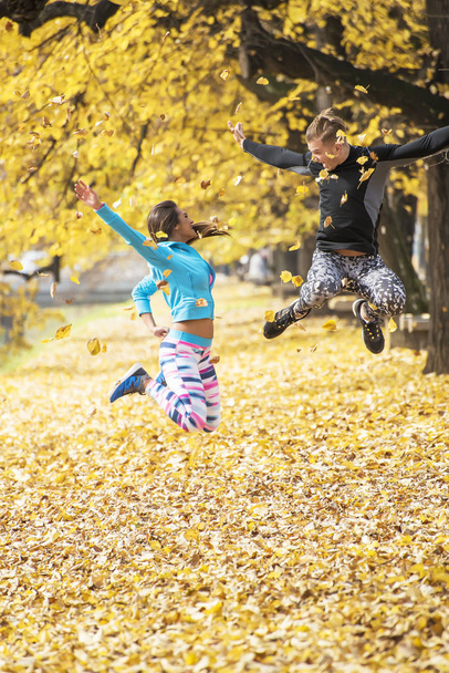 Beautiful young couple celebrate and jumping after successful training in the park. Autumn environment. - Foto, Imagem