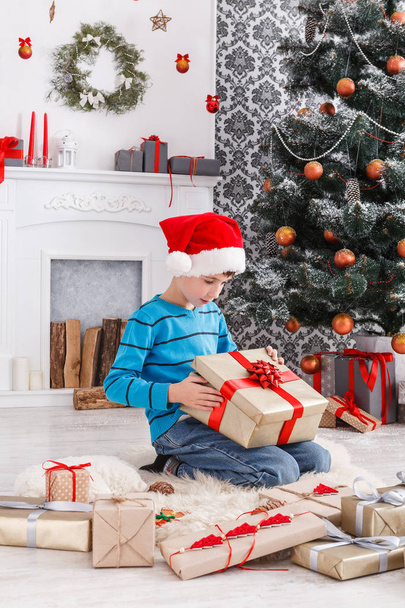 Cute boy in santa hat unwrapping christmas presents - Foto, afbeelding