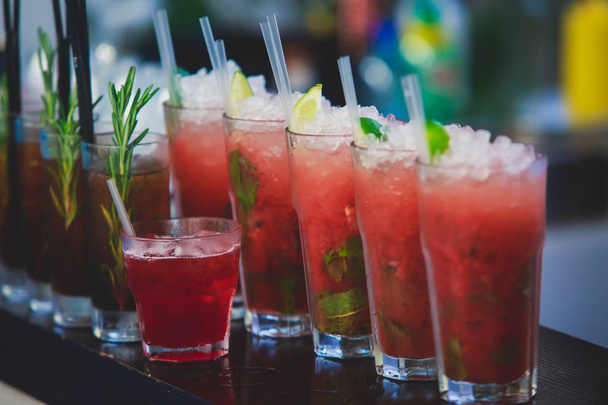 Beautiful row line of different colored alcohol cocktails on a party, martini, vodka,and others on decorated catering bouquet table on open air event, picture with beautiful bokeh - Photo, image