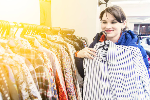 joven morena con chaqueta azul elige ropa en una tienda. Mujer compra ropa
 - Foto, Imagen