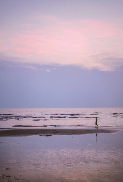 Man walking along the shoreline of beach at sunset - Photo, Image