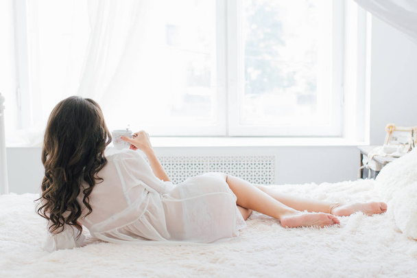 Beautiful young woman in white negligee in the morning - 写真・画像