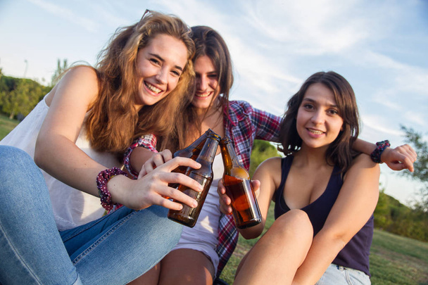 Koleżanki z okazji wakacji dobrą zabawę picie piwa w parku. Są one opiekania z butelki. - Zdjęcie, obraz