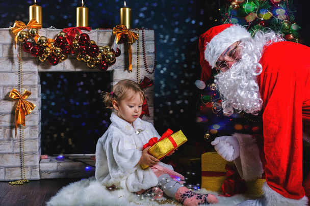 Santa and girl playing near fireplace, decorated Christmas tree - Foto, afbeelding