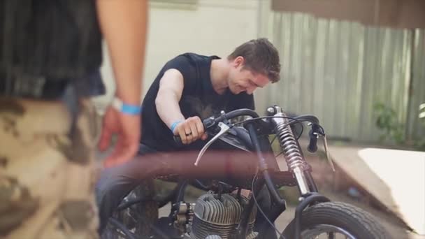 junger Mann im Hemd am selbstgebauten Motorrad. viele verschiedene ungewöhnliche Details. Sommertag. - Filmmaterial, Video