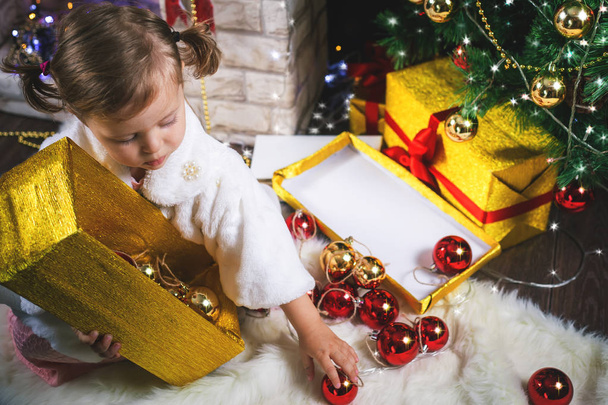 Cute toddler girl decorating a Christmas tree. Red balls. - 写真・画像