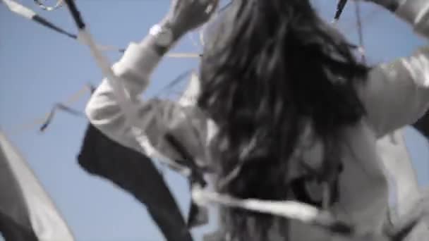 Ein fröhliches Mädchen in Kapuzenpulli und Sonnenbrille hebt die Hände zwischen schwenkenden Bändern. windiger Tag. schwarz-weiß - Filmmaterial, Video