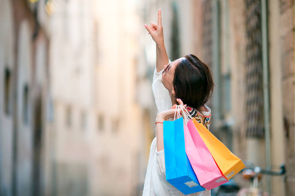 Mladá dívka s nákupní tašky na úzké uličce v Evropě. Portrét krásné šťastné ženy držící nákupní tašky s úsměvem - Fotografie, Obrázek