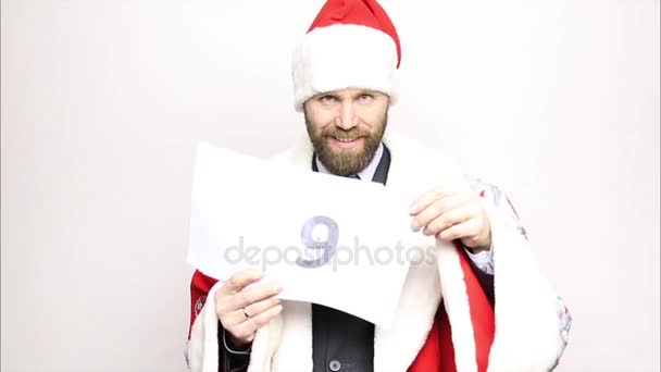 businessman in a suit of Santa Claus holds a sheet of paper with numbers. final countdown - Filmagem, Vídeo