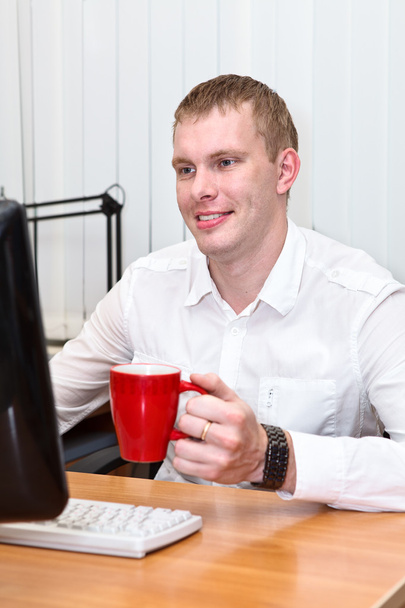 Young white collar worker with red mug in hand at working place - Foto, Imagem