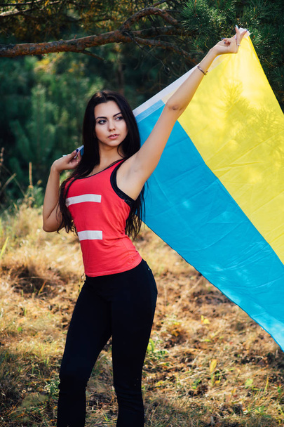 Beautiful brunette model posing in a park with  flag of Ukraine - Фото, зображення