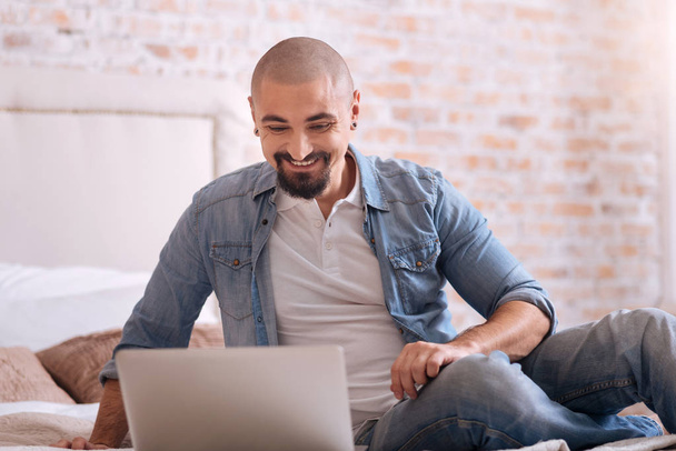 Χαμογελώντας γενειοφόρος άνδρας κάθεται μπροστά από το laptop - Φωτογραφία, εικόνα