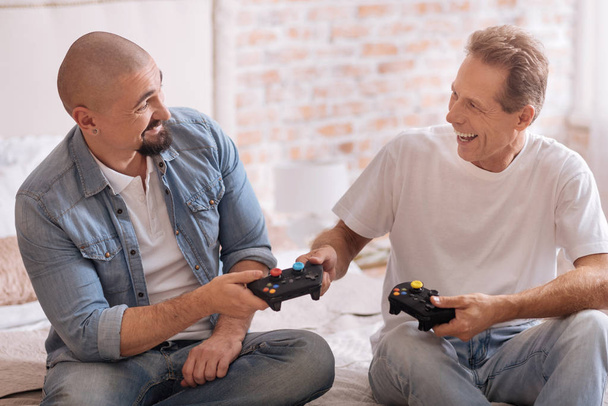 Delighted friends holding game consoles in the bedroom - Photo, image