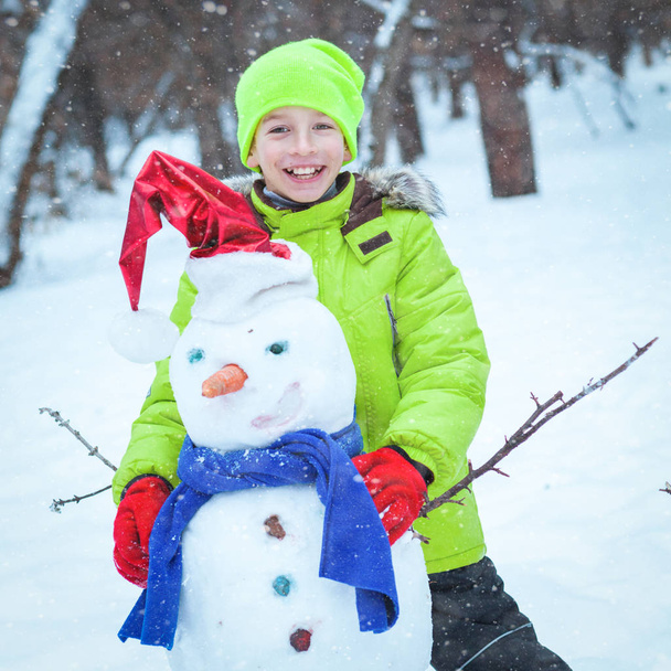 fun, happy kid playing with snowman in winter park - Фото, изображение
