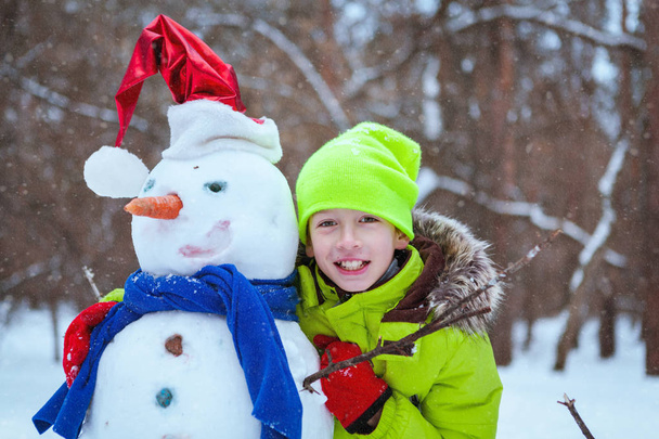 fun, happy kid playing with snowman in winter park - Fotó, kép