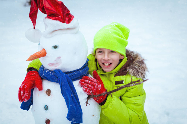 fun, happy kid playing with snowman in winter park - Foto, imagen