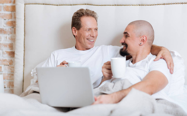 Smiling homosexual couple using the laptop in the bedroom - Valokuva, kuva