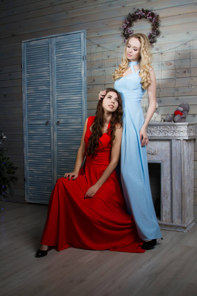 Uzun elbiseler şömineli bir odada iki genç genç kız - Fotoğraf, Görsel