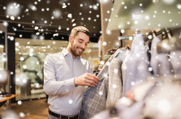 happy young man choosing clothes in clothing store - 写真・画像