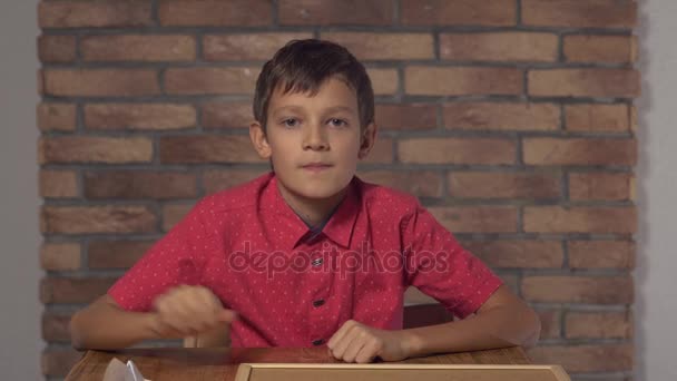 背景赤レンガの壁に旅行をレタリング フリップチャートを保持して机に座っている子 - 映像、動画