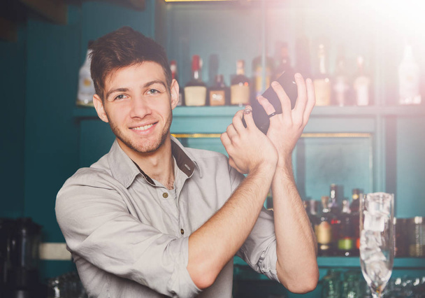 Νεαρό όμορφος μπάρμαν στο μπαρ τίναγμα και ανάμειξη αλκοόλ κοκτέιλ - Φωτογραφία, εικόνα