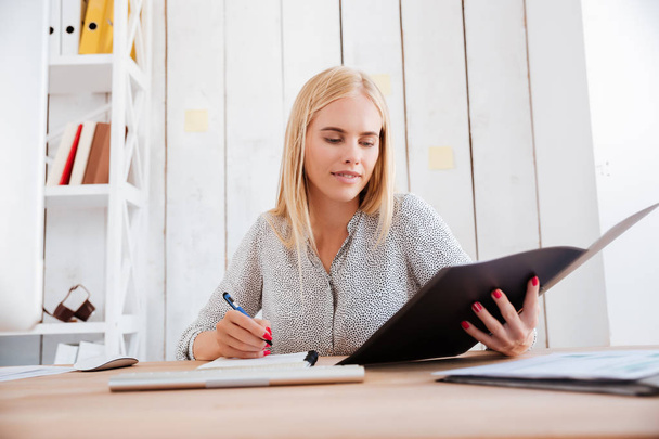 Concentrated blonde woman holding opened folder and making notes - Foto, immagini