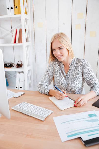 Επιχειρηματίας κάθεται στο χώρο εργασίας της και κρατώντας σημειώσεις - Φωτογραφία, εικόνα