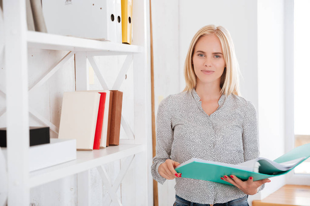 Cheerful businesswoman standing and holding folder at the office - Fotoğraf, Görsel