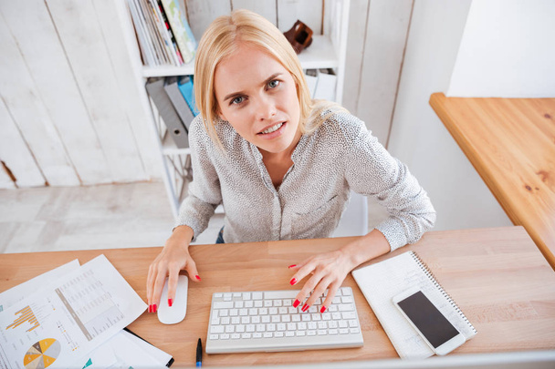 Sfrustrowany blond kobieta pracuje na komputerze i patrząc na kamery - Zdjęcie, obraz