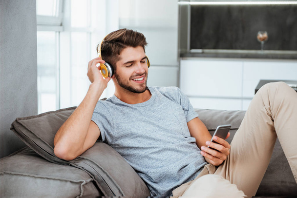 Man in headphones listening to music while lies on sofa - Foto, imagen