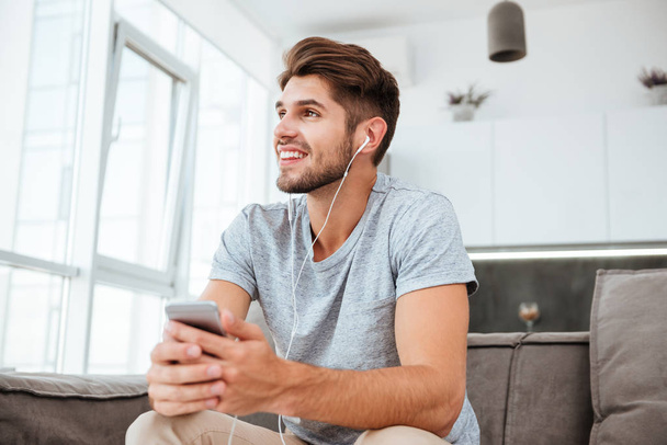 Happy man listening to music while sitting on sofa - 写真・画像