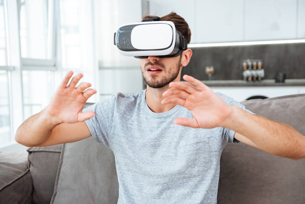 Young man wearing virtual reality device while sitting on sofa - Fotoğraf, Görsel