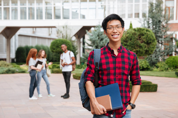 Веселий азіатський молодий чоловік студент стоїть в кампусі на відкритому повітрі
 - Фото, зображення
