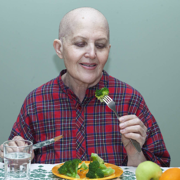 Nutrición adecuada después de la quimioterapia. Mujer calva en la mesa comiendo brócoli, fruta
 - Foto, Imagen