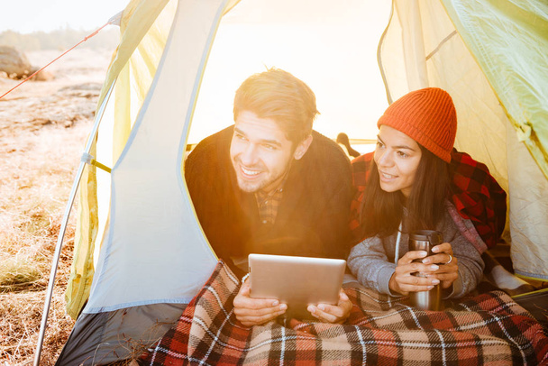 Smiling couple lying in tent and using tablet computer - Valokuva, kuva