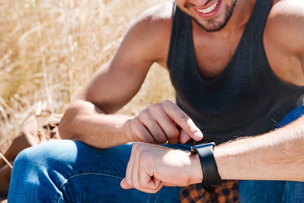 Smiling man using smart watch while sitting outdoors - Foto, Imagem
